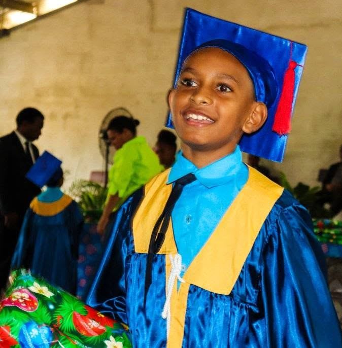 A smiling student in a blue and gold graduation gown and cap at a PMCA graduation ceremony